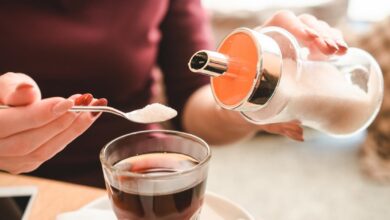 امرأة تضيف ملعقة من السكر إلى كوب شاي-التشافي بالغذاء