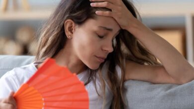 امرأة تعاني من الطقس الحار وتستخدم مروحة يدوية-التشافي بالغذاء