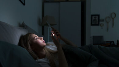 فتاة مستلقية على السرير تعاني من الأرق وتنظر في الهاتف-التشافي بالغذاء