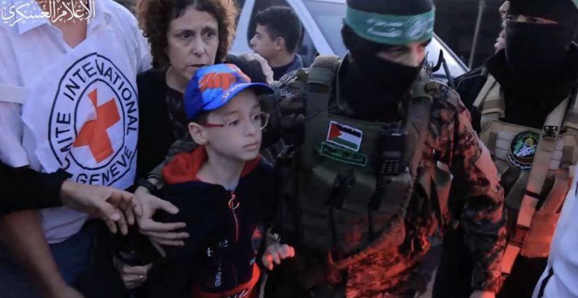 أحد عناصر كتائب القسام يرافق طفلاً من الأسرى الاسرائيلين أثناء تسليم الدفعة الثانية من الأسرى