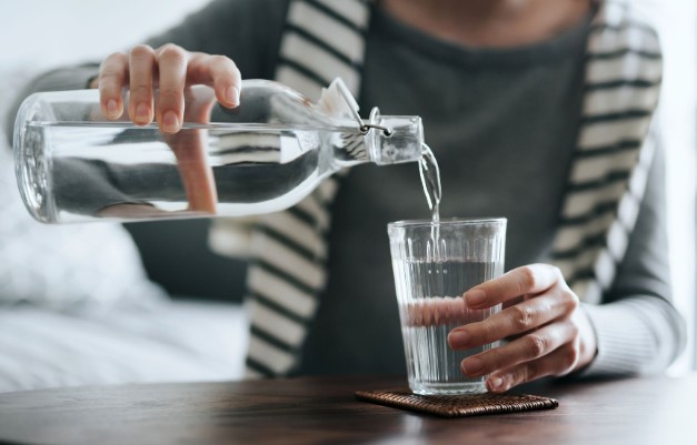 امرأة تصب الماء من الزجاجة إلى كوب زجاجي-التشافي بالغذاء