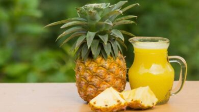 ابريق زجاجي مملوء بعصير الأناناس إلى جانب ثمرة أناناس طازجة-التشافي بالغذاء