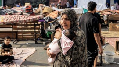 امرأة نازحة في غزة تحمل رضيعها بحثاً عن طعام-التشافي بالغذاء