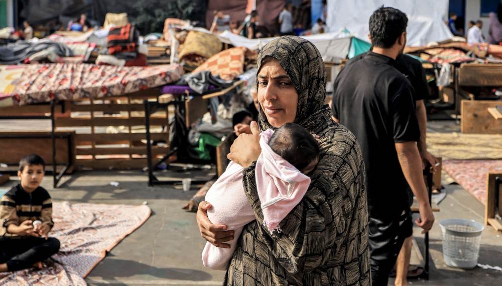 امرأة نازحة في غزة تحمل رضيعها بحثاً عن طعام-التشافي بالغذاء